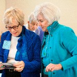 A woman is viewing pictures in her hand while another woman looks at the pictures over her shoulder